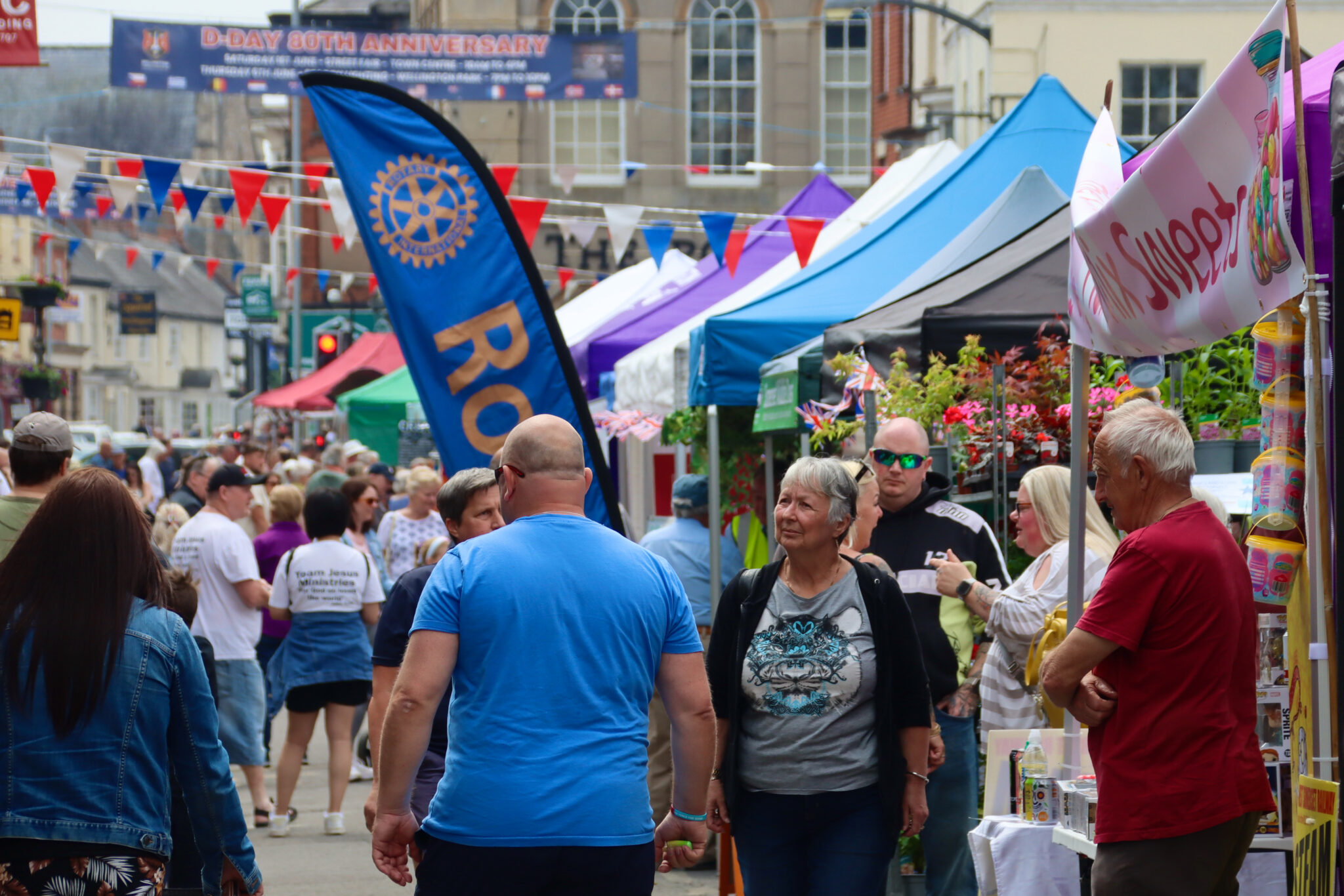 A large crowd of people in the centre of Wellington browsing stalls. Bunting runs over the streets.