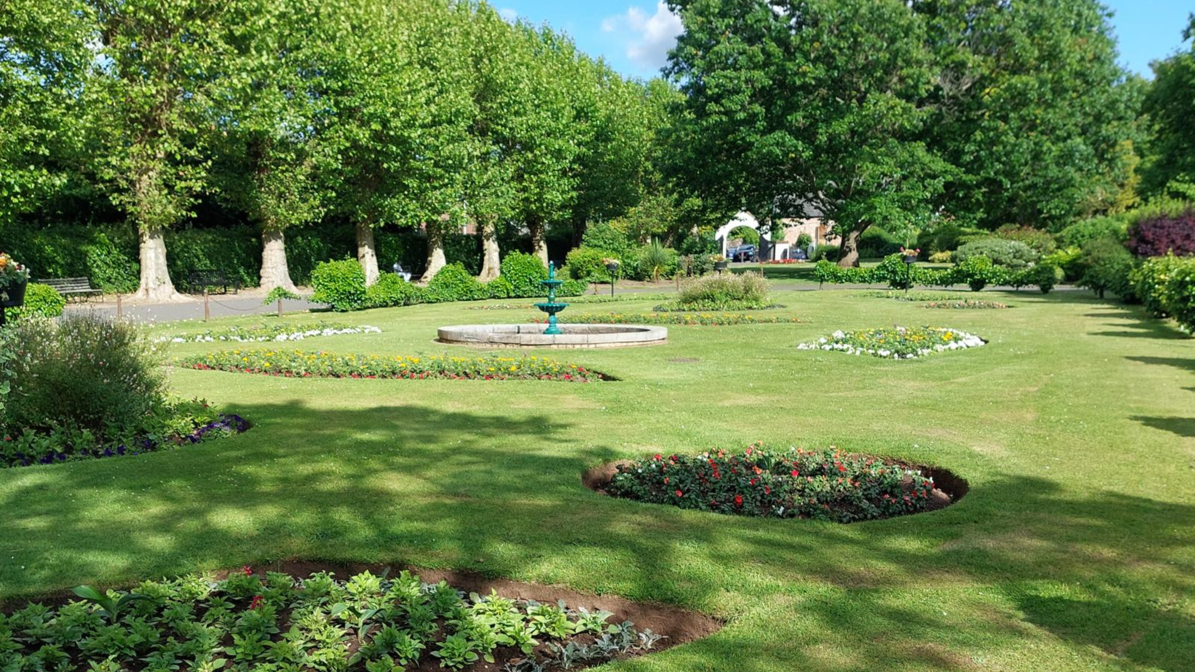 A park with a fountain in the centre of a lawn.