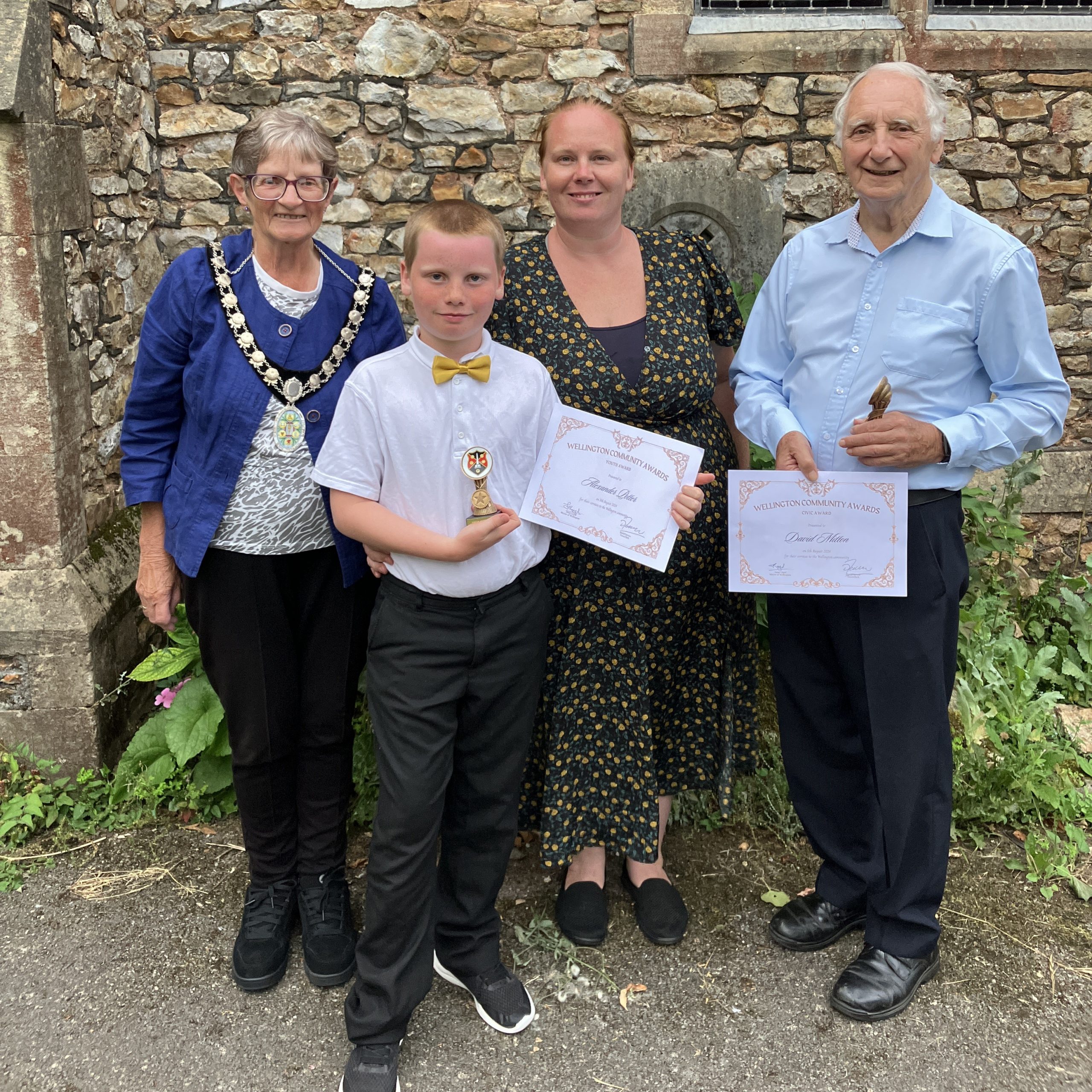 Mayor Janet Lloyd poses with two award winners who hold a certificate and trophy.