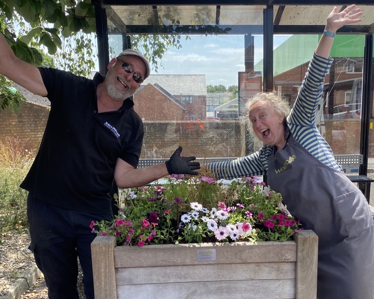 A man and woman pose joyfully with a flower planter.