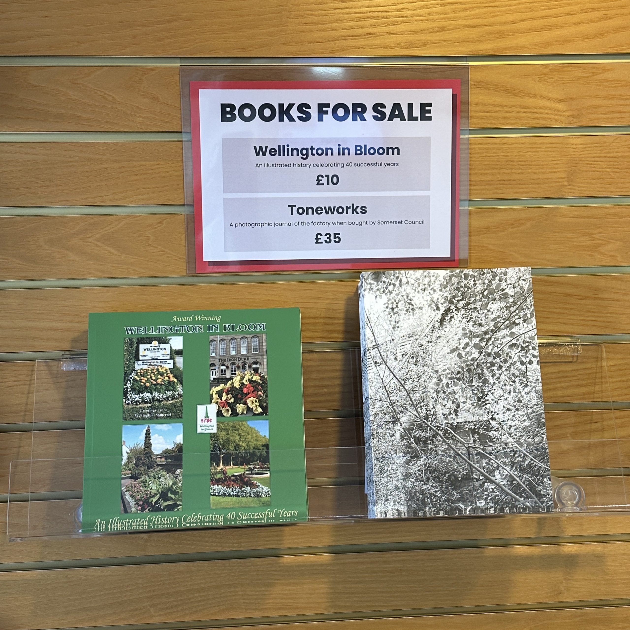 An image of two books on display. A sign above them reads "books for sale. Wellington in Bloom £10. Toneworks £35."